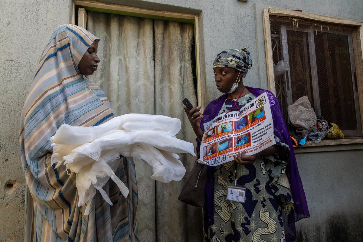 Nov. 10, 2022
(R) Umar Abdulhamid, a mosquito net mobilizer and distributor, using a chart to teach a beneficiary  how to mosquito net  during a door-to-door mosquito net distribution in Danakata, Nassarawa LGA, Kano.
As someone who has lost a loved one to malaria, Umar believes that preventing malaria is preferable to curing it, and one way to prevent malaria is through the distribution and use of mosquito nets.
Nigeria is one of the leading countries in terms of malaria cases, and Kano is one of Nigeria's largest states with a high prevalence of malaria. To combat the spread of this severe and life-threatening disease, the Global Fund, in collaboration with the Kano state government, has launched a mobilisation campaign and distributed of 8million mosquitoes to residents of the state. 
With COVID-19 still present, a door-to-door distribution system with the use of technology for implementing and tracking the distribution has been adopted in order to avoid mass gathering during net collection and to ensure effective and accountable net distribution. The field mobilisation and distribution teams were taught how to communicate with beneficiaries, keep inventory, and track distribution using the Red Rose app and the Free Net Card. Many beneficiaries are pleased with the new distribution system, which they believe is more convenient than the previous system, which required them to congregate in a congested area to collect their nets.